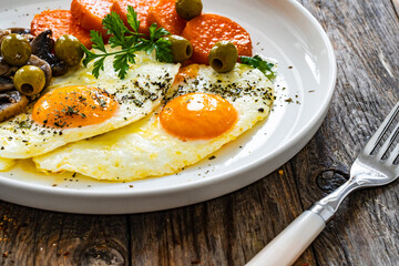 Breakfast - sunny side up egg, toasted bread, sweet potato, mushrooms  and olives served on wooden table
