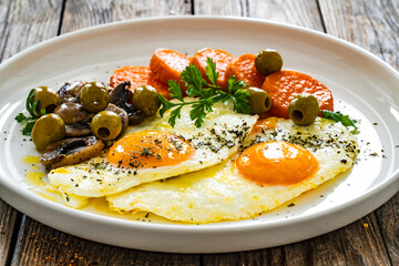 Breakfast - sunny side up egg, toasted bread, sweet potato, mushrooms  and olives served on wooden table
