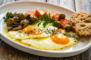 Breakfast - sunny side up egg, toasted bread, sweet potato, mushrooms  and olives served on wooden table
