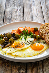Breakfast - sunny side up egg, toasted bread, sweet potato, mushrooms  and olives served on wooden table

