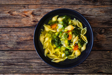 Pistou soup Nice - broth with basil pesto, noodles and vegetables on wooden background in black bowl