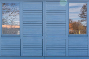 blue wooden facade of building with two windows with reflections of nature on both sides