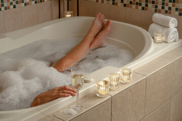 Woman Relaxing in the Bathroom Spa Tub with a Glass of Sparkling Champagne and Candles.