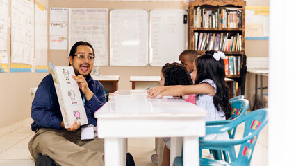 Hispanic adult male teacher holding a book and teach a preschool children.