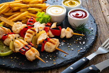 Meat skewers - grilled meat with French fries and fresh  vegetables on wooden background
