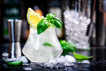 Summer icy cocktail drink with mezcal, liqueur, sugar syrup, lemon, juice, green basil, spices and crushed ice, dark bar counter background - 783906169