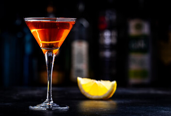 Orange alcoholic hard cocktail drink with scotch whiskey, vermouth and liquor in martini glass, dark bar counter background - 783906173