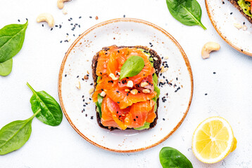 Avocado and salmon toast on rye bread with spinach, cashew and sesame seeds, white table background, top view - 783906344
