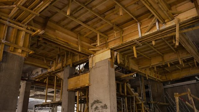 Construction site with wooden scaffolding for ceiling support. Wooden roof framework of unfinished building. Overview of beams inside building under construction