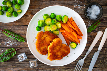Crispy breaded fried pork loin chops with sweet potato fries and boiled Brussels sprouts on wooden...