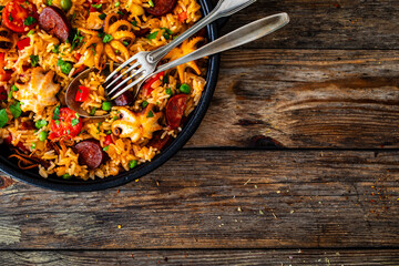 Paella seafood and chorizo in cooking pan on wooden table
