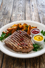 Grilled beef sirloin steak with baked potatoes on wooden table
