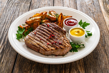 Grilled beef sirloin steak with baked potatoes on wooden table
