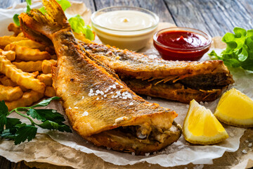Fried perch with French fries and lemon served on paper on wooden table

