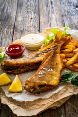 Fried perch with French fries and lemon served on paper on wooden table

