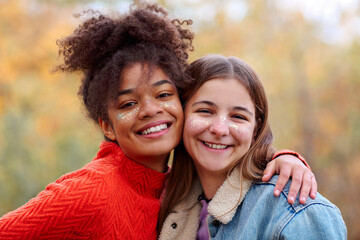 Two happy multiracial girlfriends smiling at camera and hugging while standing in autumn forest
