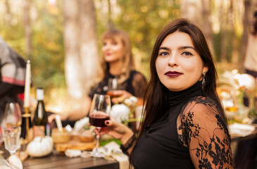 Portrait of beautiful woman with evening makeup in black dress sitting with friends at table outside