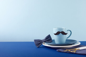Classy father's day table setting with mug and bow tie. Side view against a blue background with...