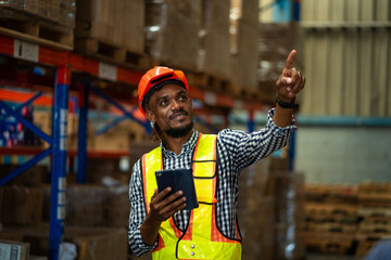 A man in a safety vest is pointing at something on a tablet. He is wearing a hard hat and is...