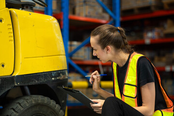 A woman in a safety vest is sitting on the ground and writing on a clipboard. She is inspecting a...