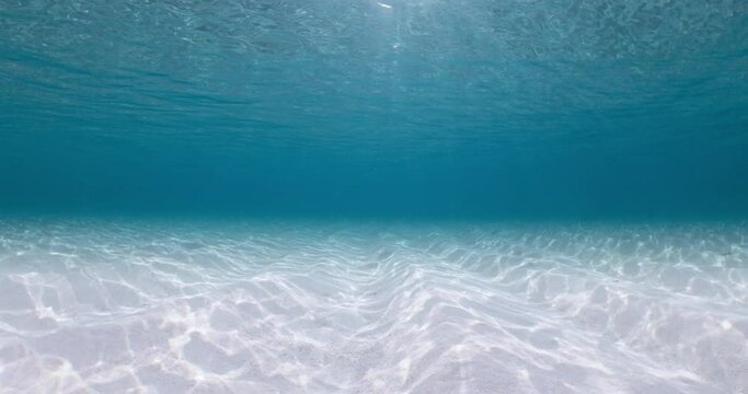 Transparent turquoise ocean with sandy sea bottom and sunlight in Bahamas. Underwater view background