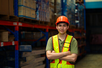 A man in a safety vest stands in a warehouse. He is wearing a hard hat and is smiling