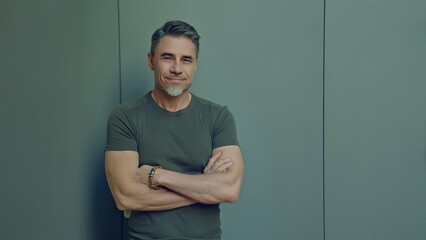 Portrait of a smiling middle aged man standing arm crossed confidently. Happy mid adult male in casual. Blank copy space on a gray wall background.