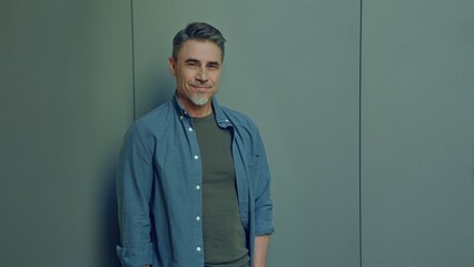 Portrait of a smiling older man with casual style standing. Happy, confident mid adult male in casual. Blank copy space on a gray wall background.