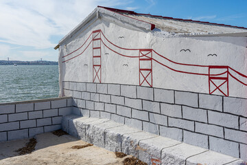House with painted wall with the bridge 25 de Abril dd Lisbon seen from the city of...