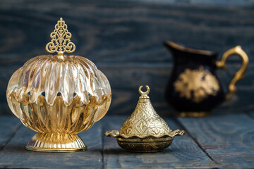 Golden ornate bowl with lid off and smaller container in background.