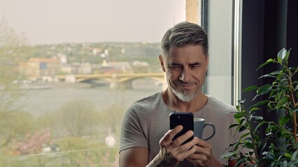 Man drinking morning coffee using phone at home