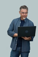 Casual mid adult man standing holding laptop computer. Portrait of happy middle aged male in 50s with gray hair and glasses, smiling. Isolated on white background. - obrazy, fototapety, plakaty