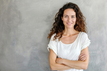 Portrait of a smiling confident woman in her forties, with crossed arms in front of a grey wall background