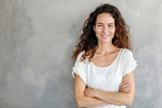 Portrait of a smiling confident woman in her forties, with crossed arms in front of a grey wall background