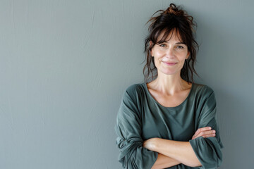 Portrait of a smiling confident woman in her forties, with crossed arms in front of a grey wall...