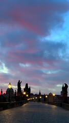 Fototapeta na wymiar Prague's Charles Bridge at dawn: Street lights gleaming under pink-grey skies.
