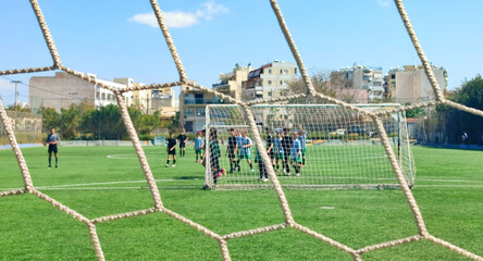 Photo of a kids Sunday football league match behind a goal net. Conceptual image.

