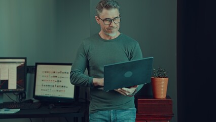 Older man working with laptop computer in home office. Mid adult male in glasses, happy, smiling, looking busy. Casual entrepreneur, businessman in small business office.