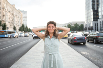 Urban environment. Car and city noise. A girl stands against the backdrop of the city, frowns and...