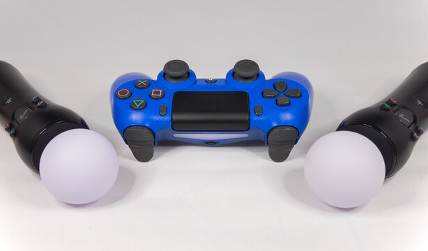 Blue Playstation 4 controller with Move controllers lit up against a white background. London - 22nd April 2020