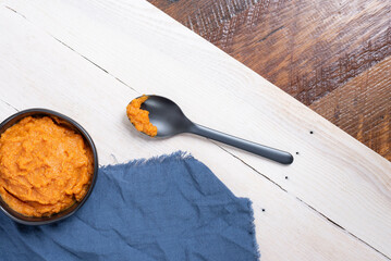 Black bowl with fresh cooked pumpkin, whitewashed tray on wooden table.  Spoon with bite of pumpkin, dark blue cloth.