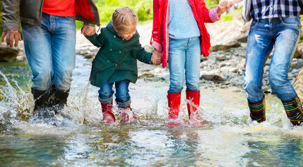 Happy family wearing rain boots jumping into a mountain river