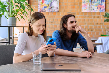Young people, couple man and woman relaxing together in cafe, using smartphone