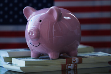 PClose up pink piggy bank with US Dollar bills against flag of United States as symbol of economy, business and investment of USA.