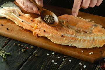 Chef hands use a spoon to add coriander to the fish carcass on the cutting board with spices. Concept of preparing fish dish in tavern kitchen