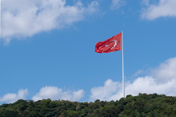 a large flag of Turkey waving on a white flagpole on a hillside with trees on a blue day, copy space