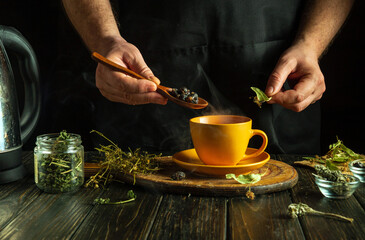 The cook brews healthy tea from medicinal dry herbs. A hand holds a spoon with dry rosehips that...