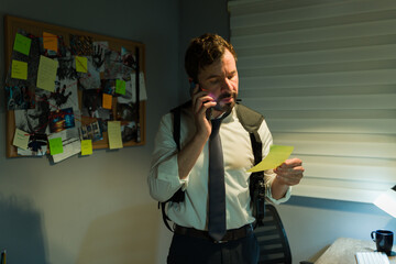 Pensive detective on the phone gathers clues, with a corkboard of evidence behind him
