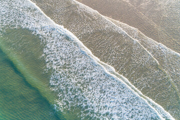 waves of a turquoise sea reaching the shore of a beach in summertime, top view with drone