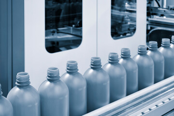 A row of plastic bottles on a conveyor belt. The bottles are all the same color and are lined up in...